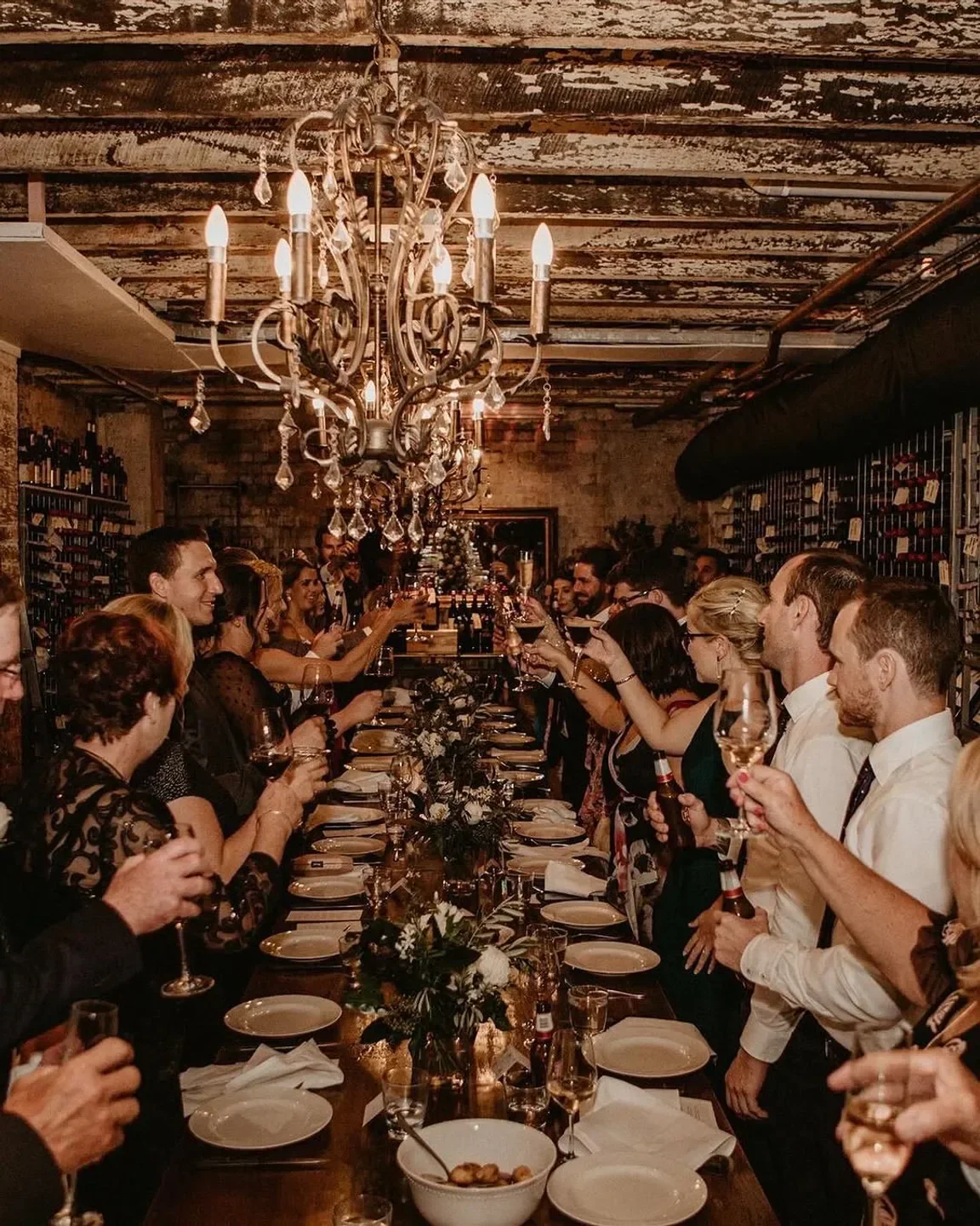 Celebration inside 1889 Enoteca, Brisbane restaurant with a grand chandelier and wine glasses.