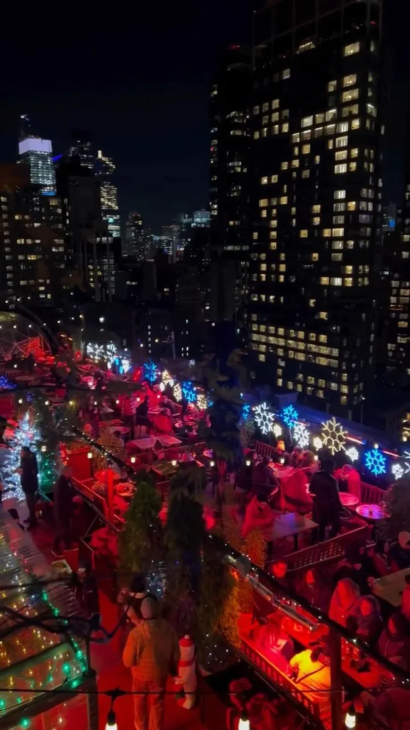 Festive snowflake lights illuminate the bustling 230 Fifth Rooftop bar in New York City at night.