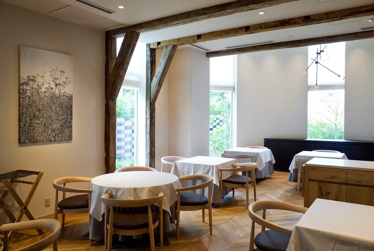 Elegant dining area at Ad Hoc restaurant in Osaka, featuring wooden beams and round tables.