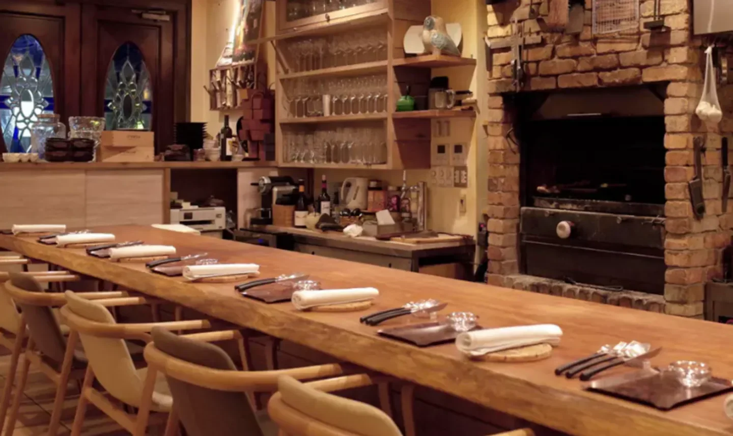 Interior of Alarde restaurant in Osaka, showcasing a long wooden table and brick oven.