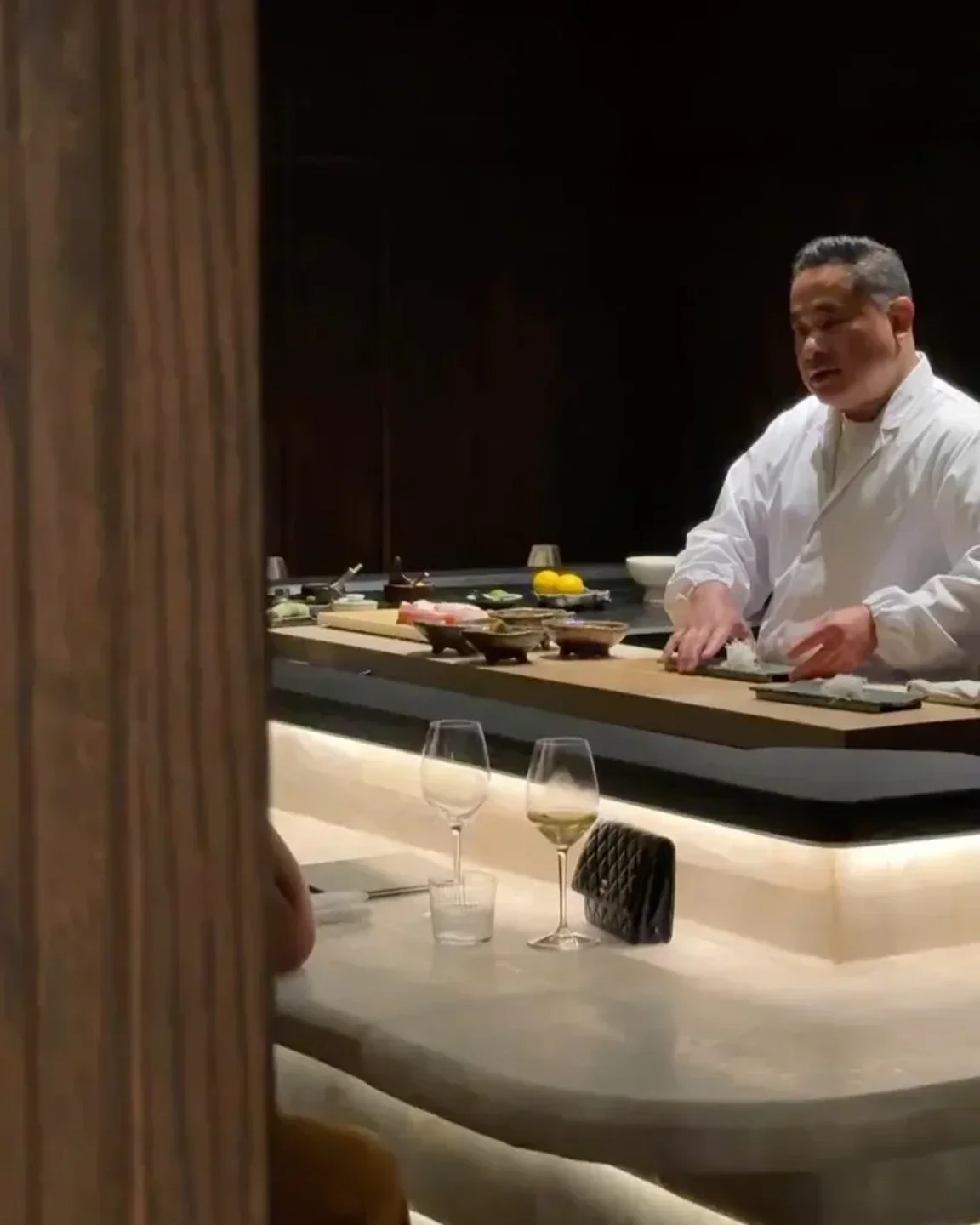 Chef at AMA Sushi Santa Barbara preparing sushi at the bar with wine glasses.