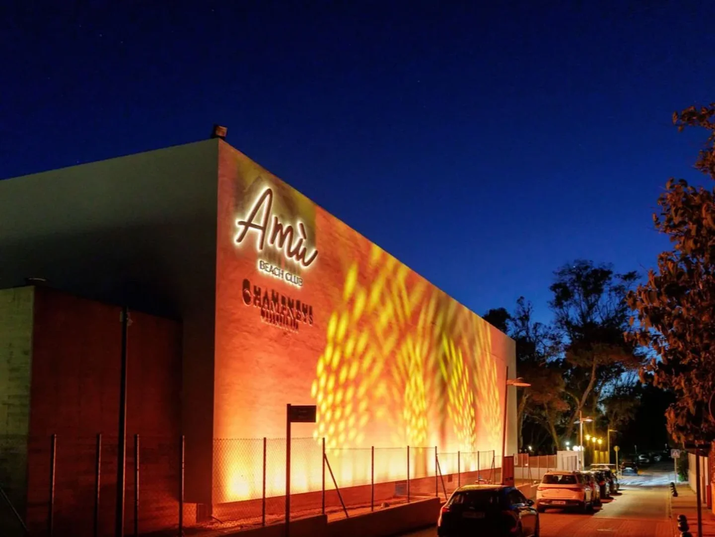 Amu Beach Club in Marbella illuminated at night with vibrant orange and yellow lights on the exterior wall.