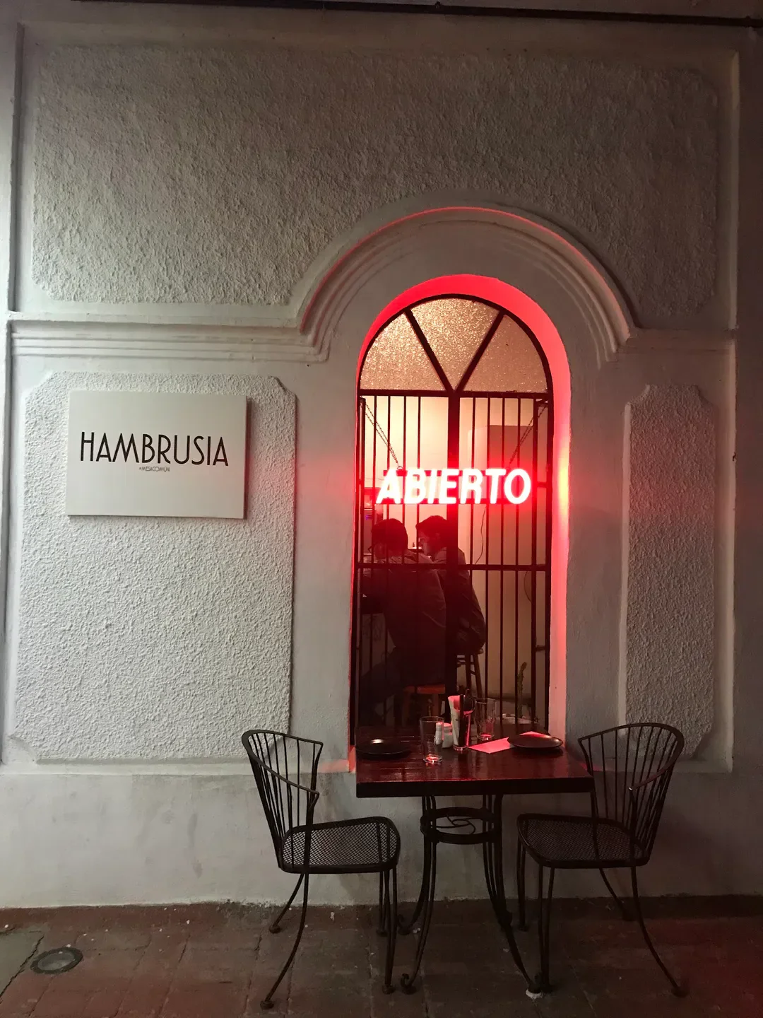 Cozy outdoor dining at ARAMI restaurant in La Paz, with red neon 'Abierto' sign.