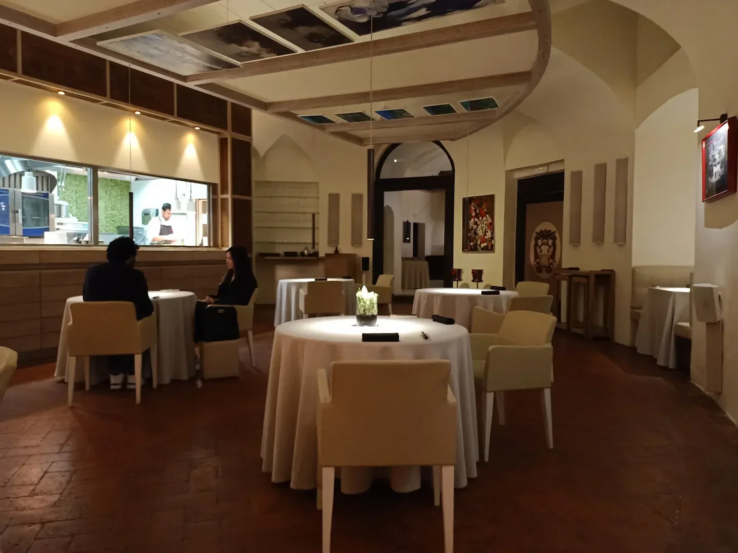 Elegant interior of Atman a Villa Rospigliosi restaurant in Tuscany, with patrons and kitchen view.