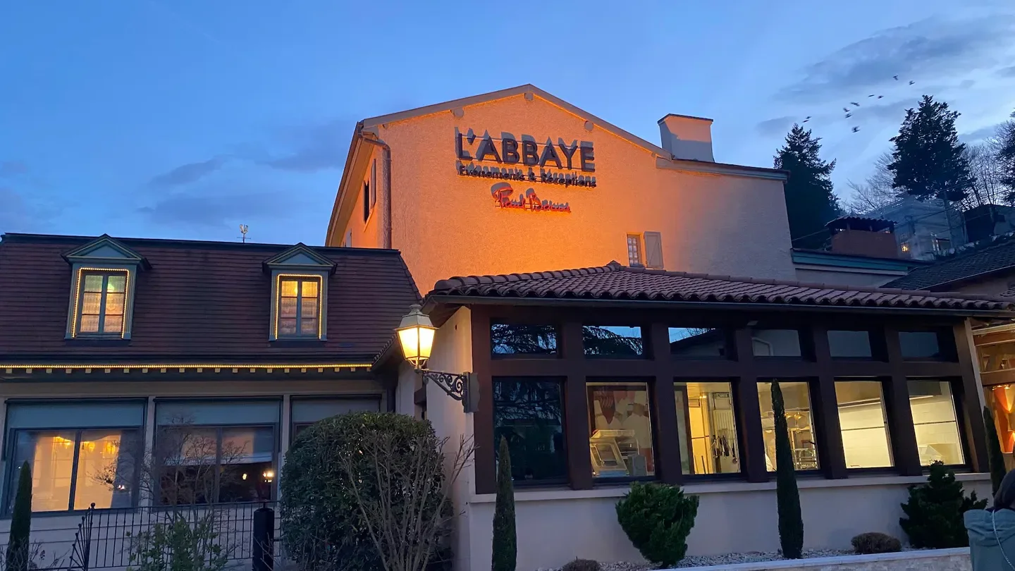 Exterior of Auberge de l'Abbaye restaurant in Lyon at dusk with illuminated sign
