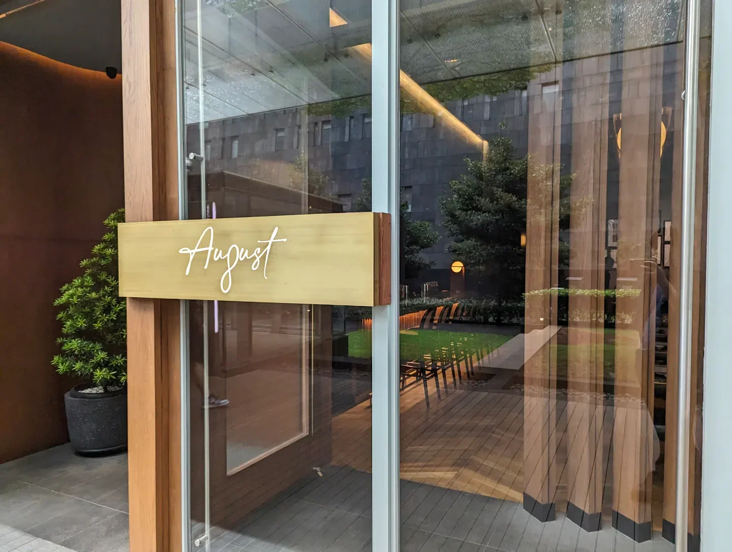 Entrance of August restaurant in Jakarta featuring a sleek sign and outdoor seating.