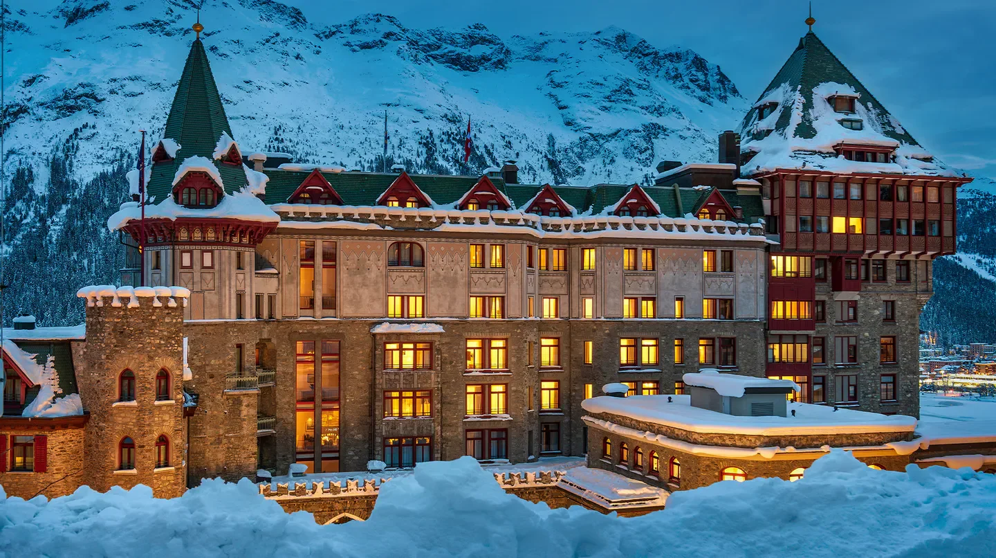 Badrutt's Palace Hotel in St. Moritz at dusk, covered in snow with mountains