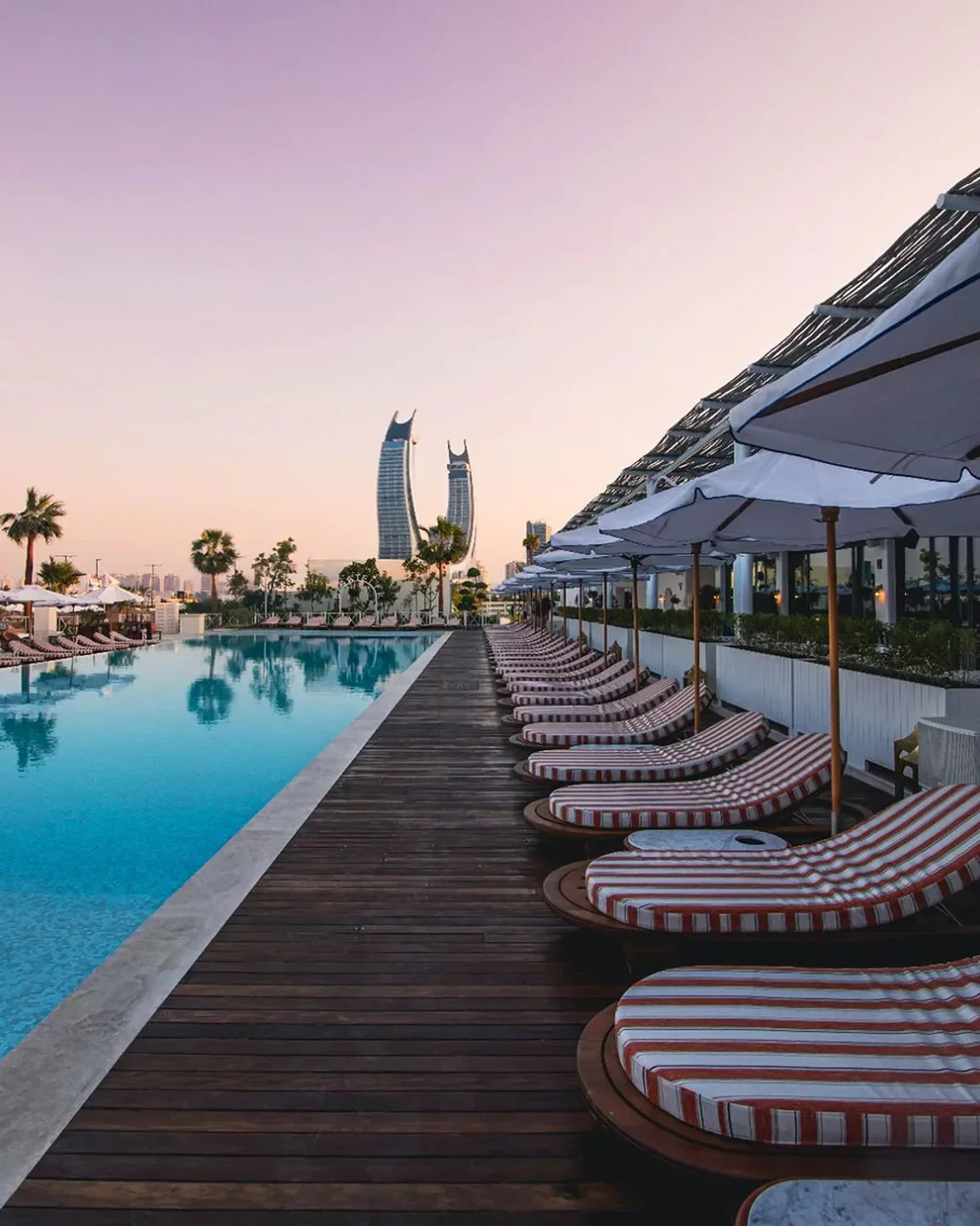 Bagatelle Beach Doha's elegant pool deck with striped loungers, umbrellas, and city skyline.