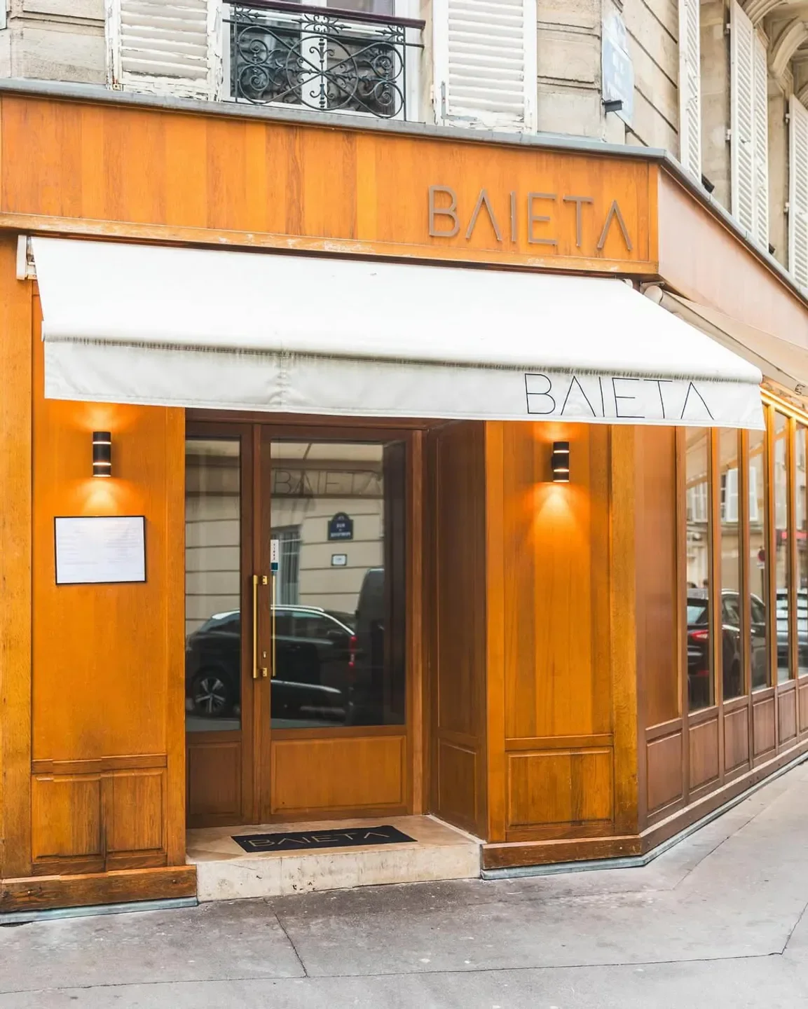 Entrance of Baieta restaurant in Paris, with wooden facade and white awning.