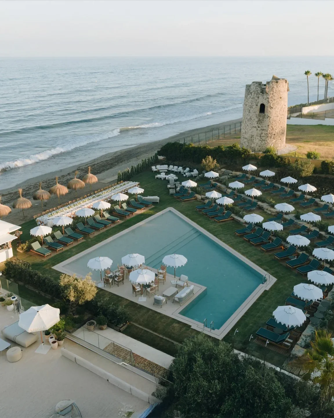 Barbillón Marbella luxury beach club exterior with pool, sunbeds, umbrellas, and historic tower by the sea