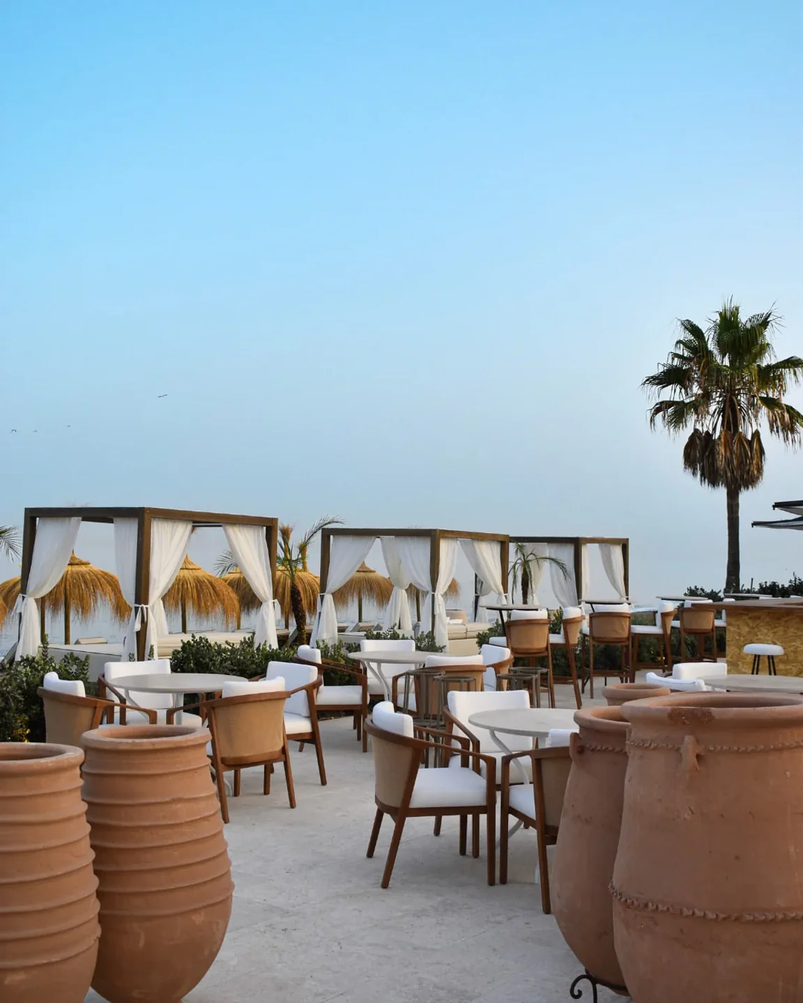 Outdoor seating area at Barbillón restaurant in Marbella with beach cabanas and palm trees