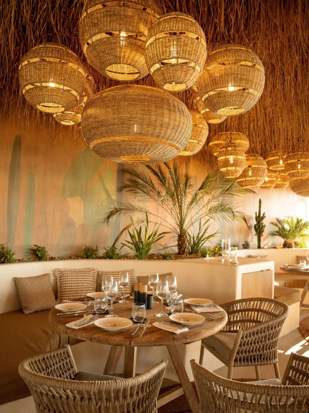 Woven pendant lights and palm trees in the tropical interior of Beefbar Santorini restaurant.