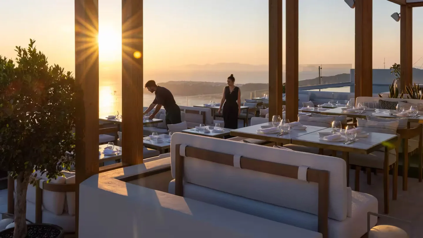 Elegant outdoor dining setting at Blu restaurant in Santorini during a golden sunset with sea views.