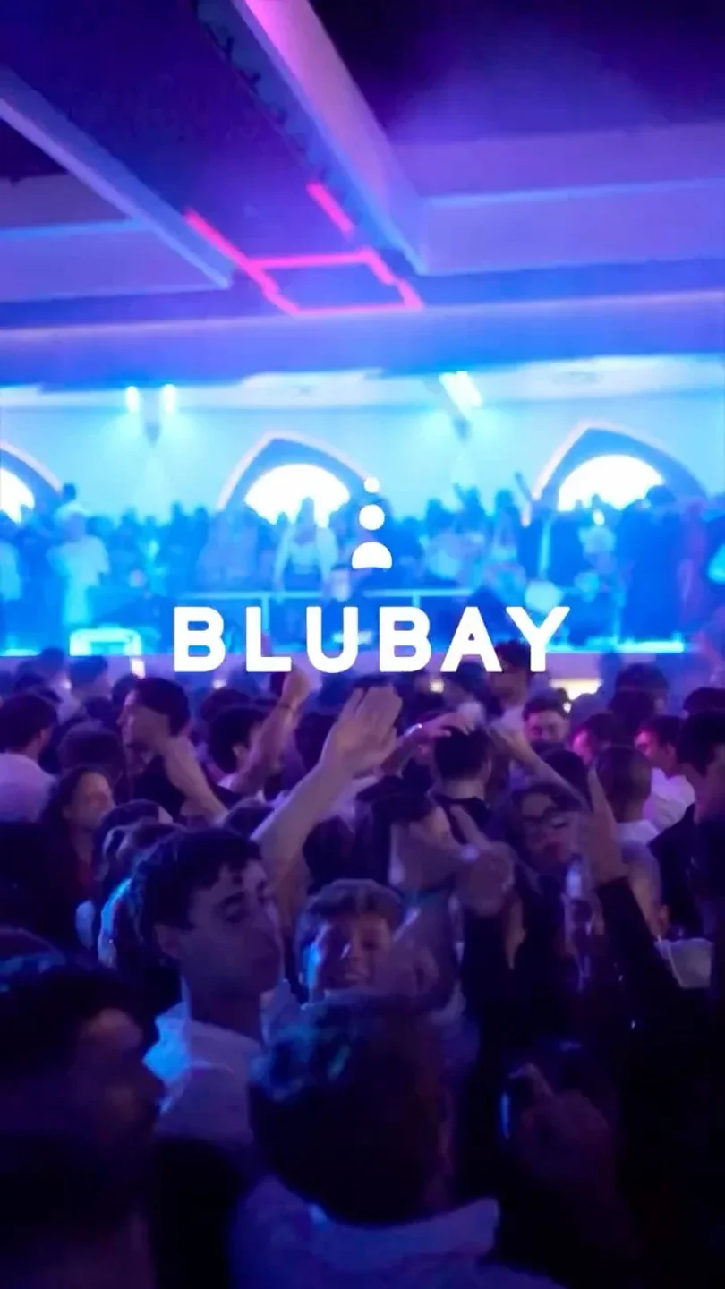 Energetic crowd dancing under vibrant blue and purple lights at Blubay Club in Puglia.