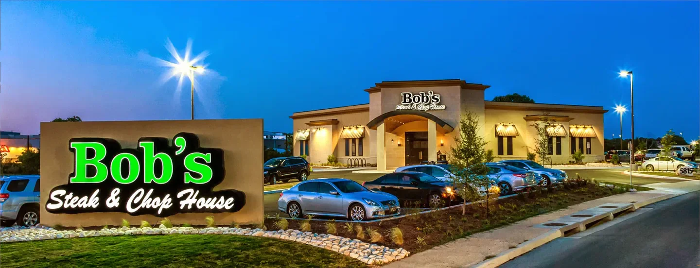 Exterior view of Bob's Steak & Chop House in San Antonio at dusk with cars parked out front.