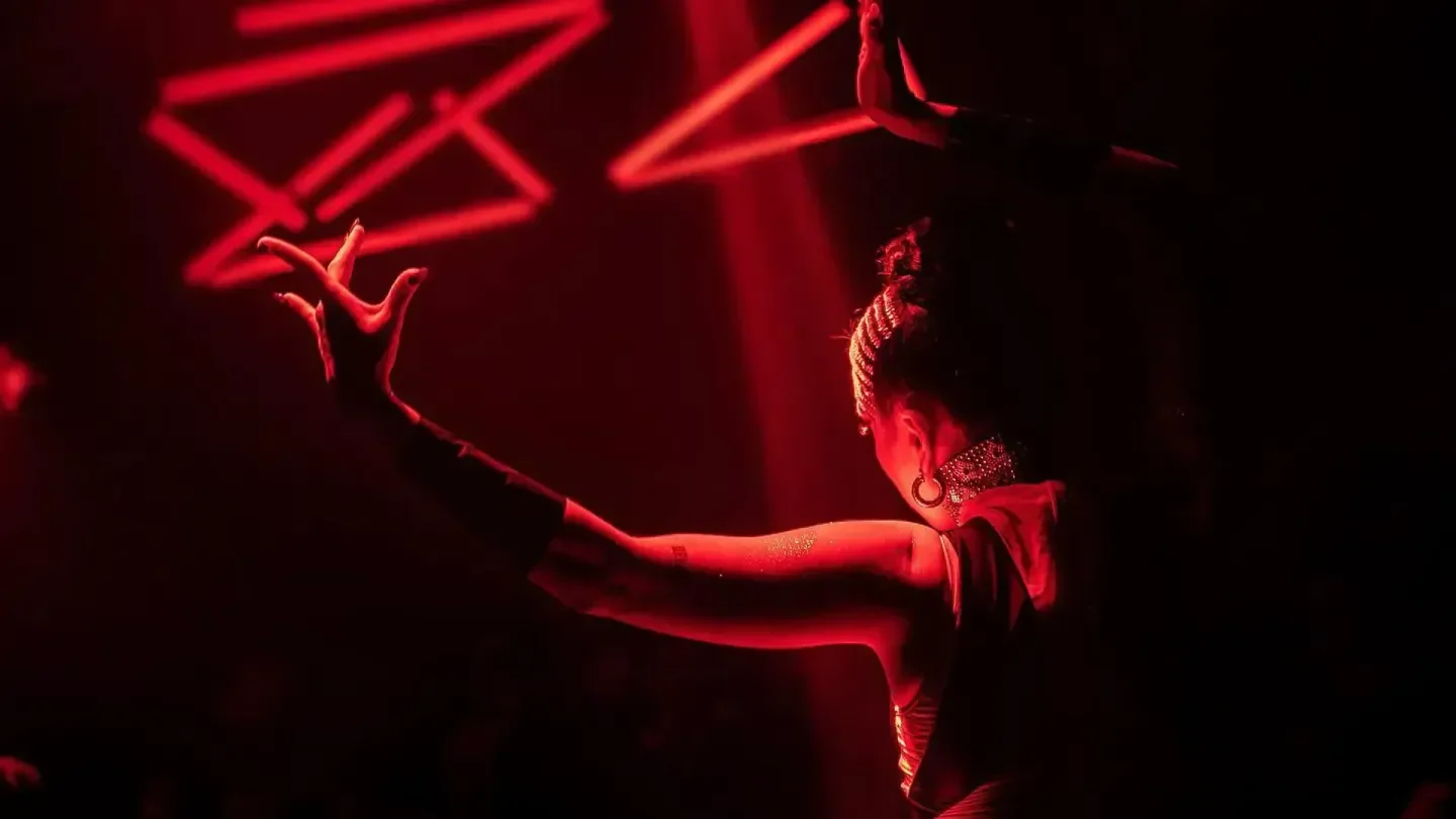 Dancer in red light at Bonbonnière Tulum nightclub, hands gracefully outstretched.