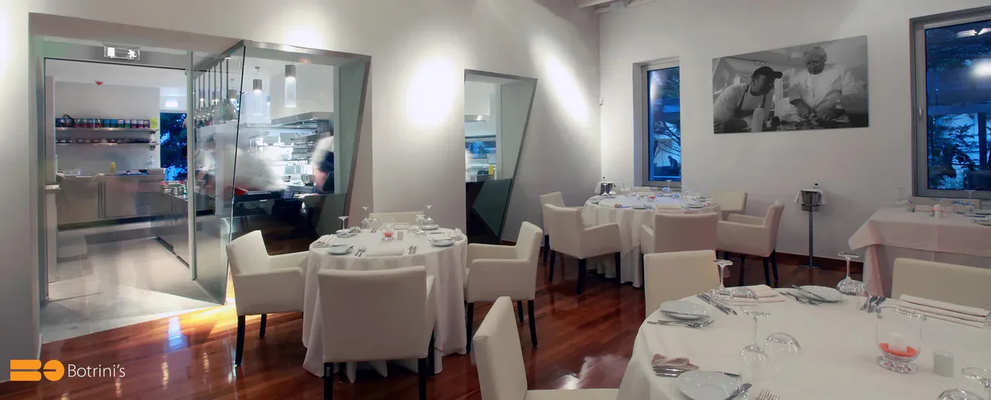 Elegant dining room interior at Botrini's restaurant in Athens, with a glimpse of the kitchen