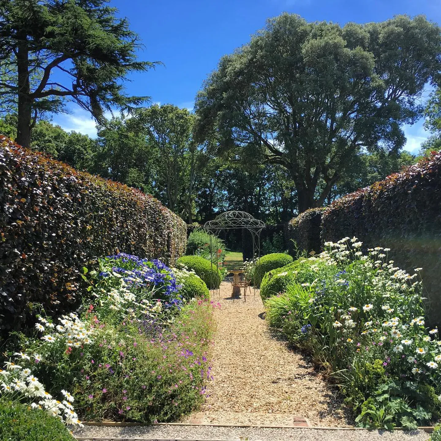 Beautiful garden path at Buckland Manor in the Cotswolds, lined with flowers and trimmed hedges.
