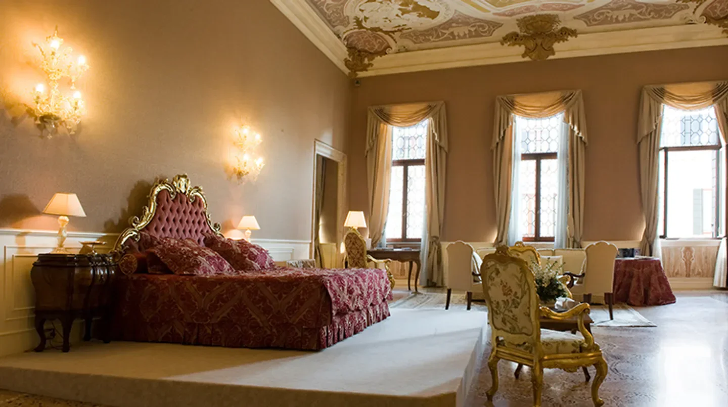 Elegant bedroom at Ca' Sagredo Hotel in Venice with antique furniture and ornate ceiling.