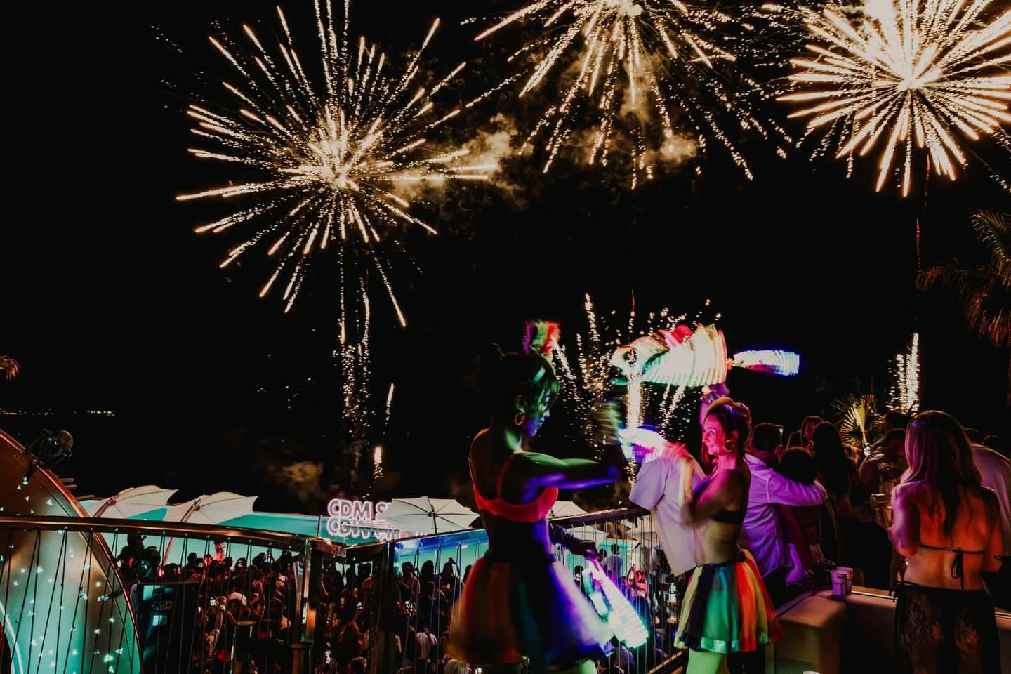 Vibrant fireworks explode over Café del Mar Malta as people enjoy a lively beach club atmosphere.