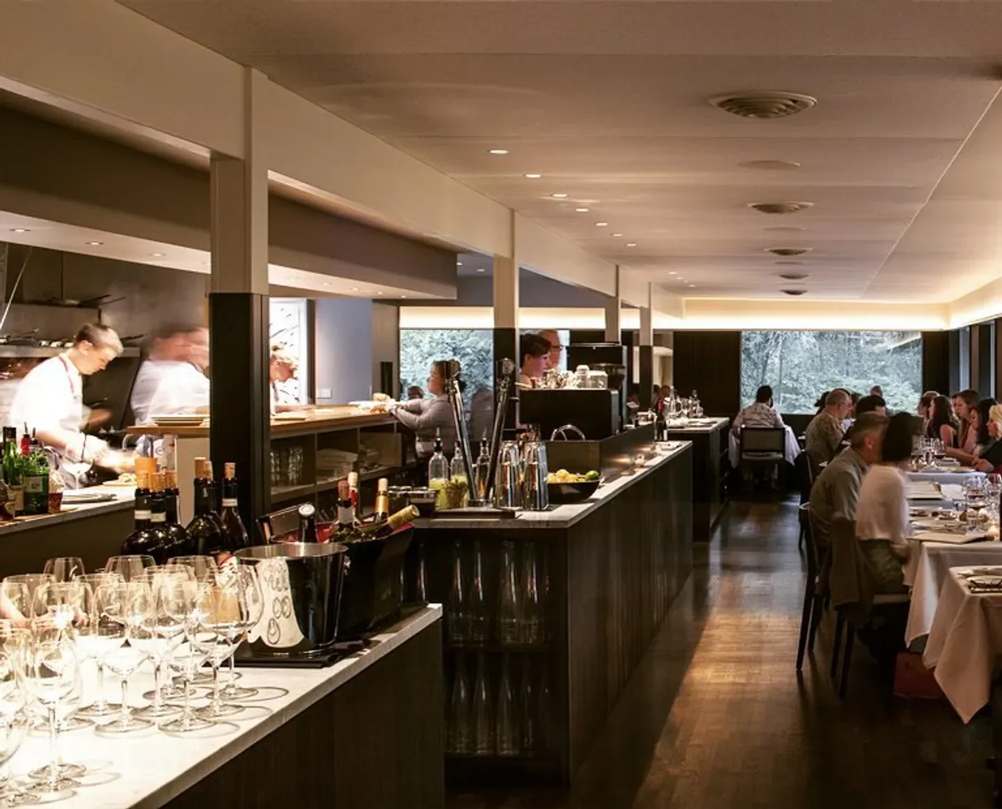 Interior of Cafe Juanita in Seattle featuring dining tables and busy kitchen staff.