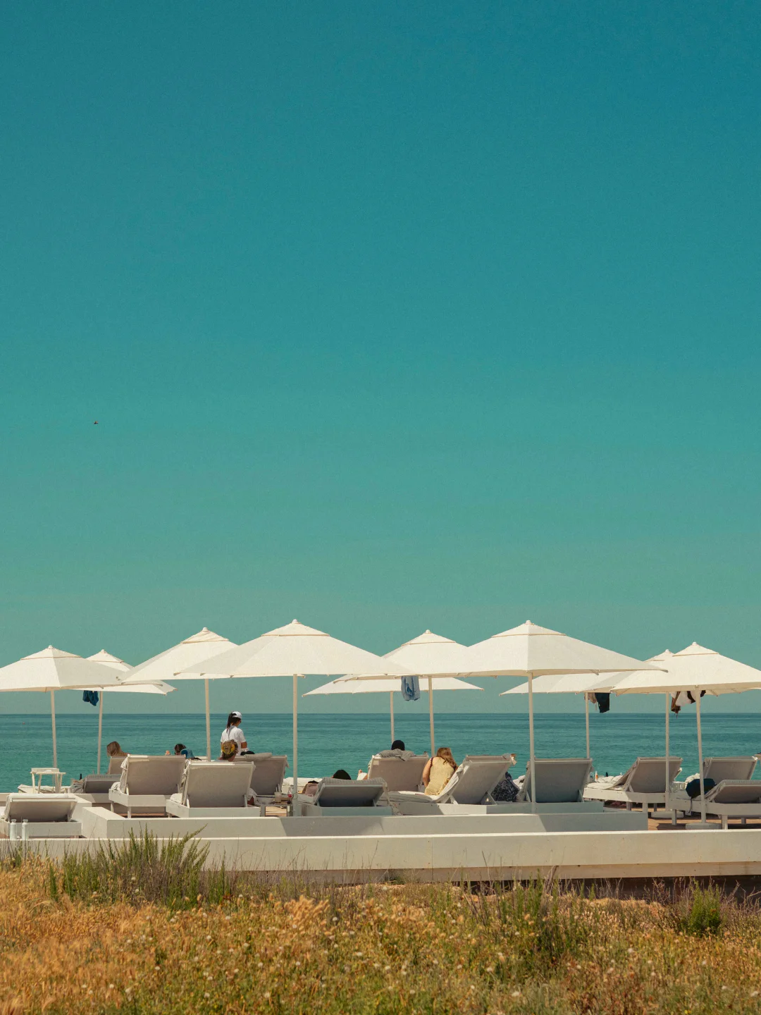 Cala Masciola beach club in Puglia with white umbrellas and lounge chairs by the sea