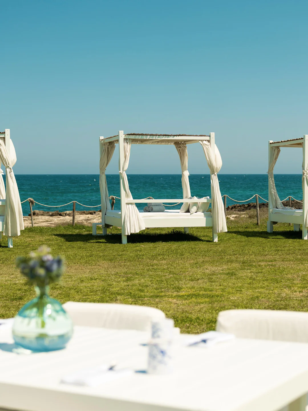 White cabanas with curtains set on lush green grass overlooking the turquoise sea at Cala Masciola, Puglia.