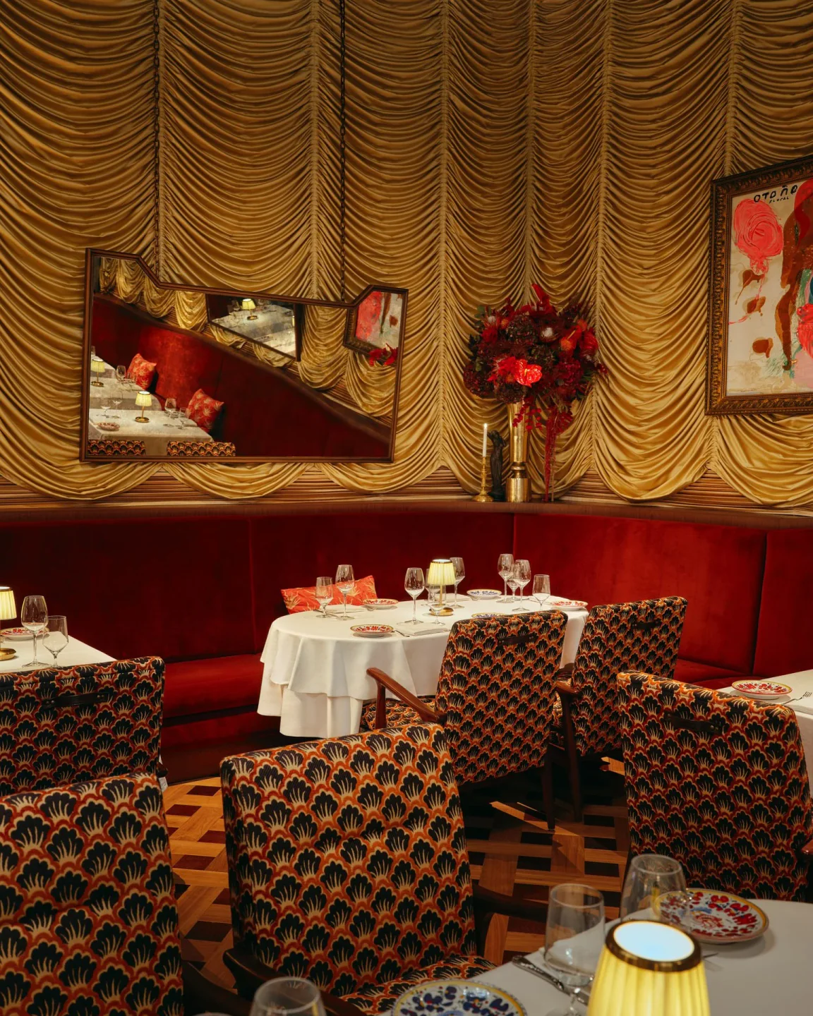 Carbone restaurant interior featuring plush red banquettes, golden drapes, and unique patterned chairs in the city.