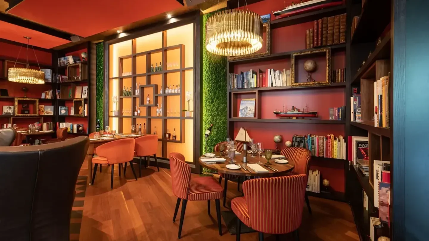 Cozy restaurant interior at Carlton Zurich, featuring bookshelves and elegant dining tables.