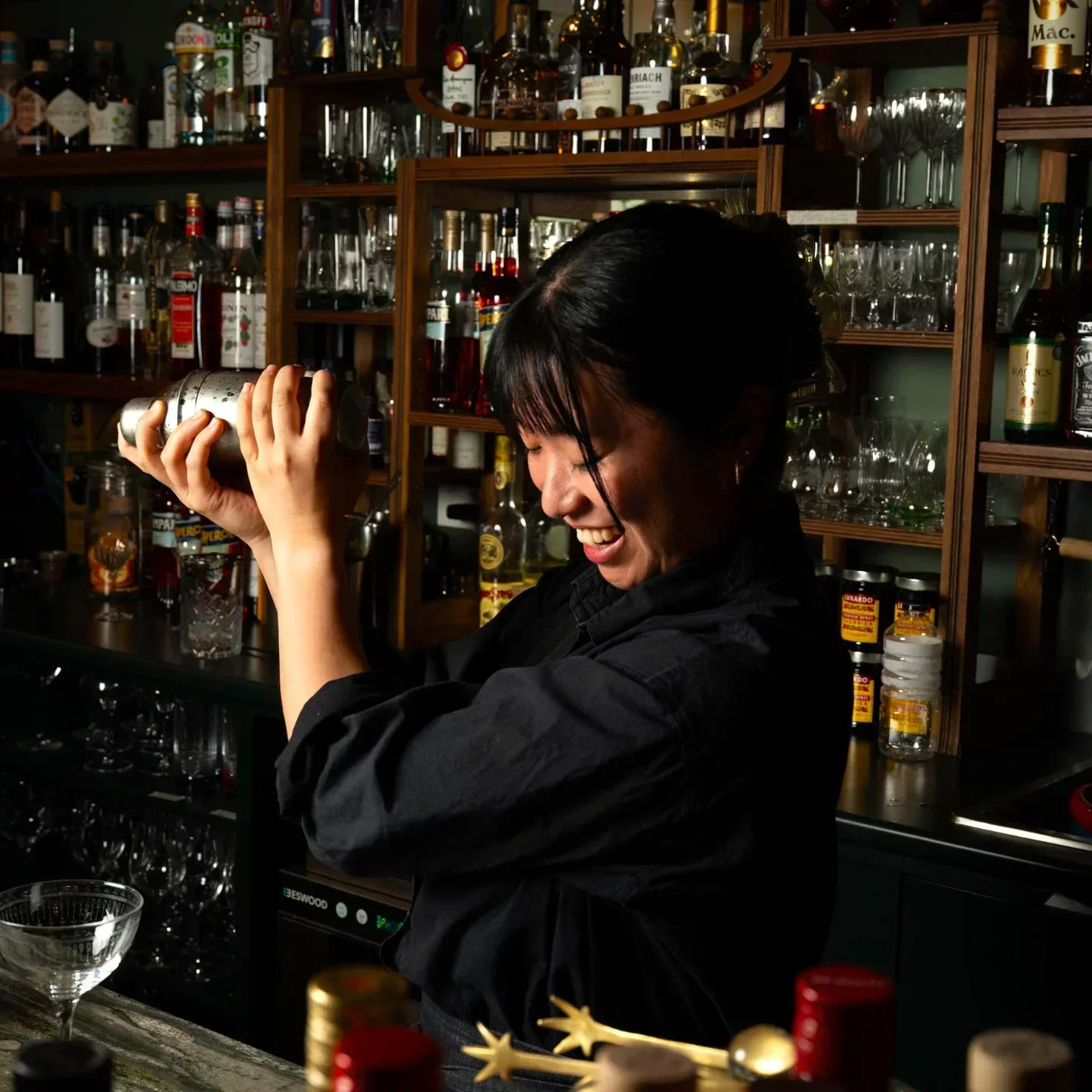 Enthusiastic bartender at Caruggi Geelong shaking cocktail, with shelves of liquor in background.
