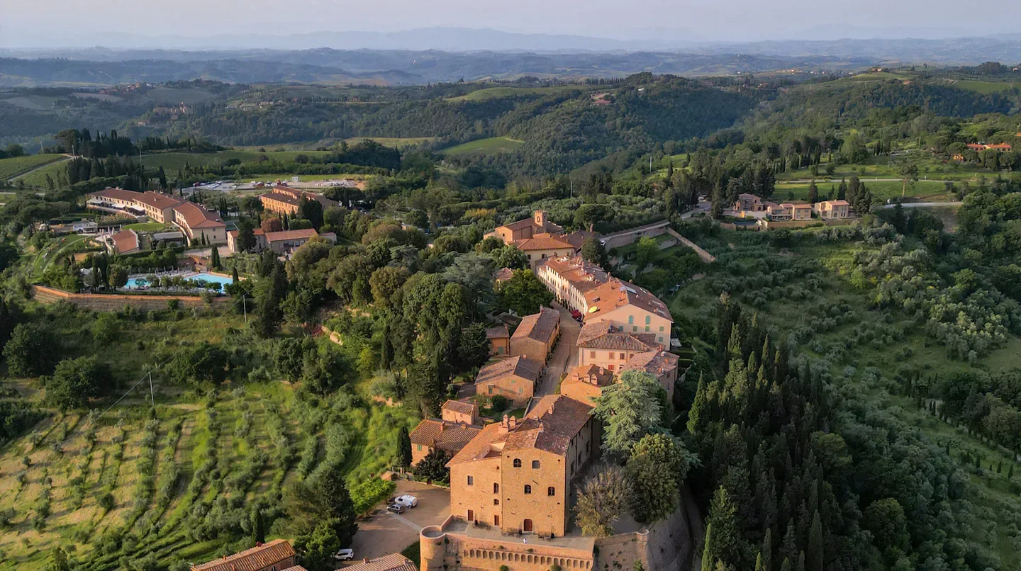Aerial view of Castelfalfi Hotel in Florence, Italy, surrounded by rolling hills and trees.