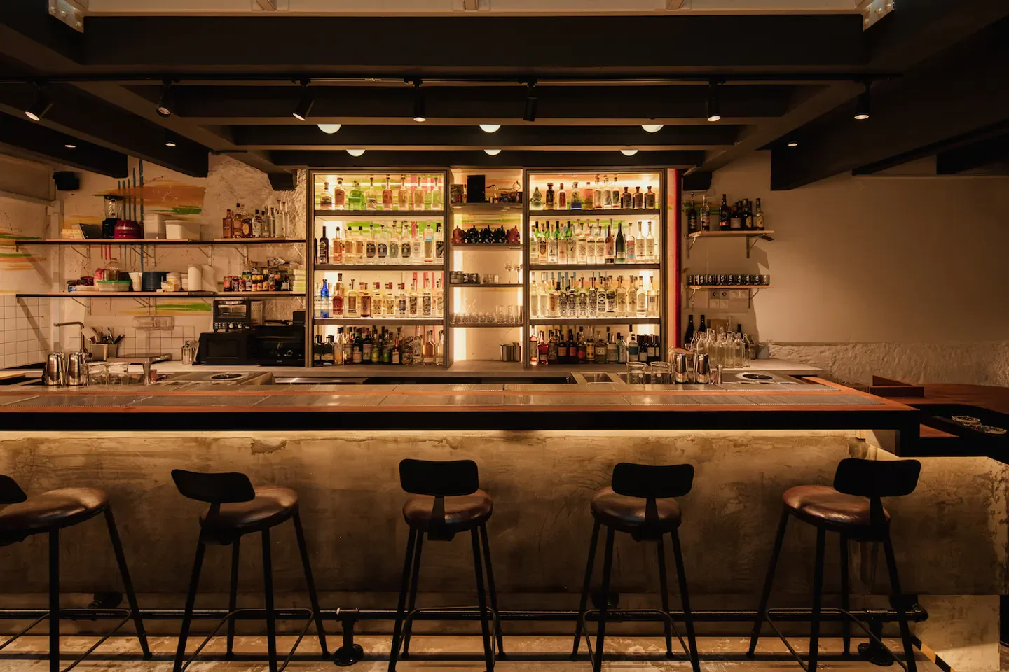 Interior view of the bar at Cat Bite Club in Singapore, with bottles and stools.