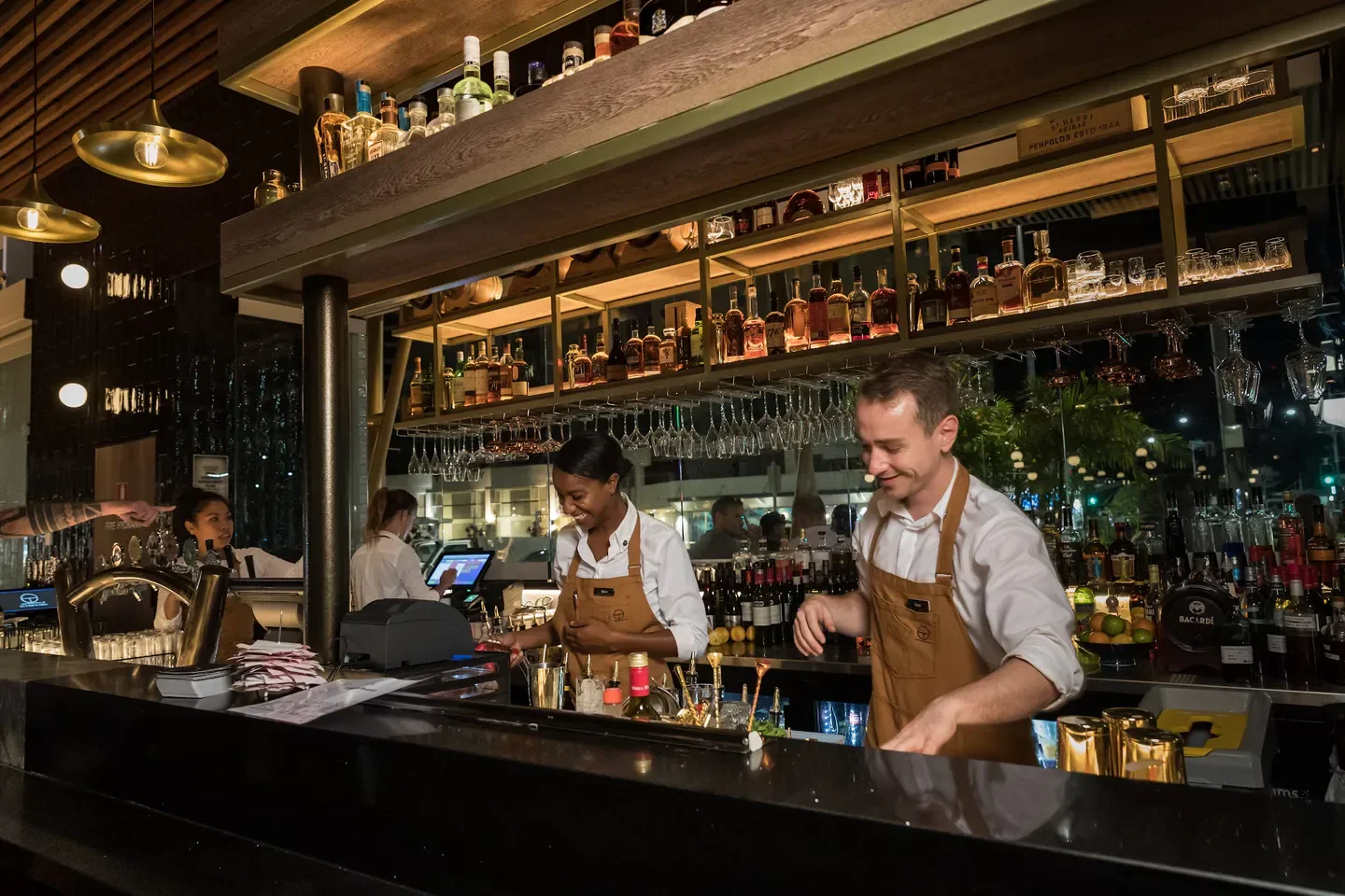 Busy bar at CC's Bar & Grill in Cairns, with bartenders preparing drinks for customers.