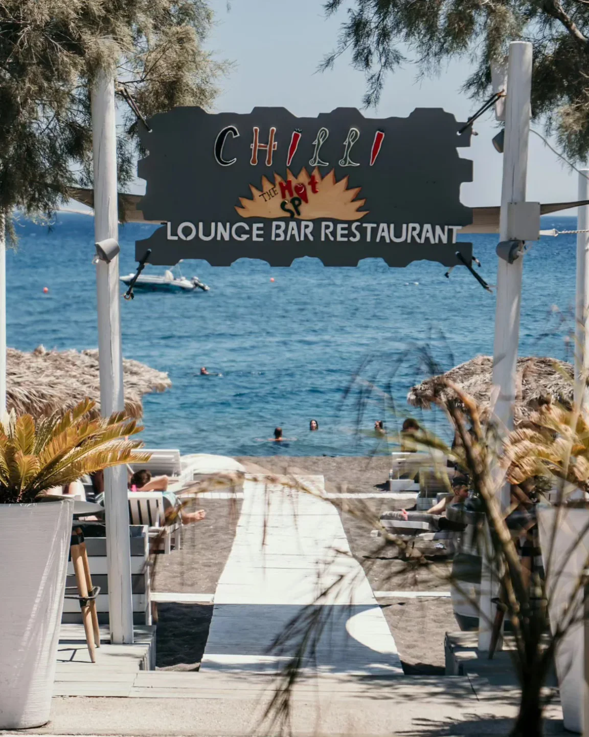 Chilli Beach Bar lounge exterior in Santorini with a pathway to the black sand beach and blue sea.