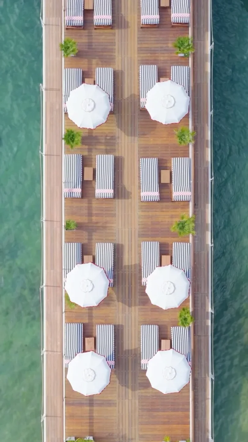 Ciro's beach club in Cannes features striped loungers and white umbrellas on a wooden deck overlooking clear blue water.