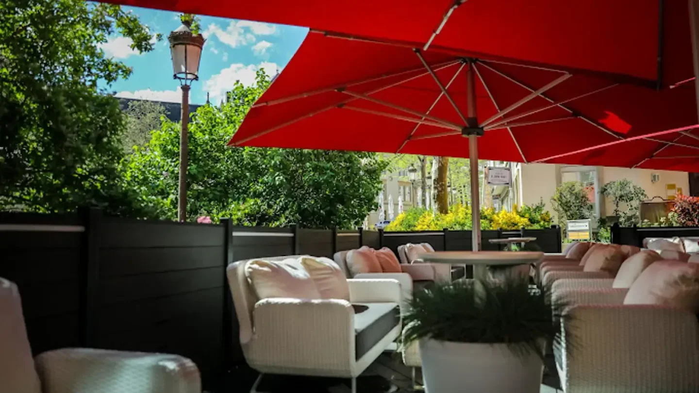 Outdoor seating at Clairefontaine restaurant in Luxembourg with red umbrellas and greenery.