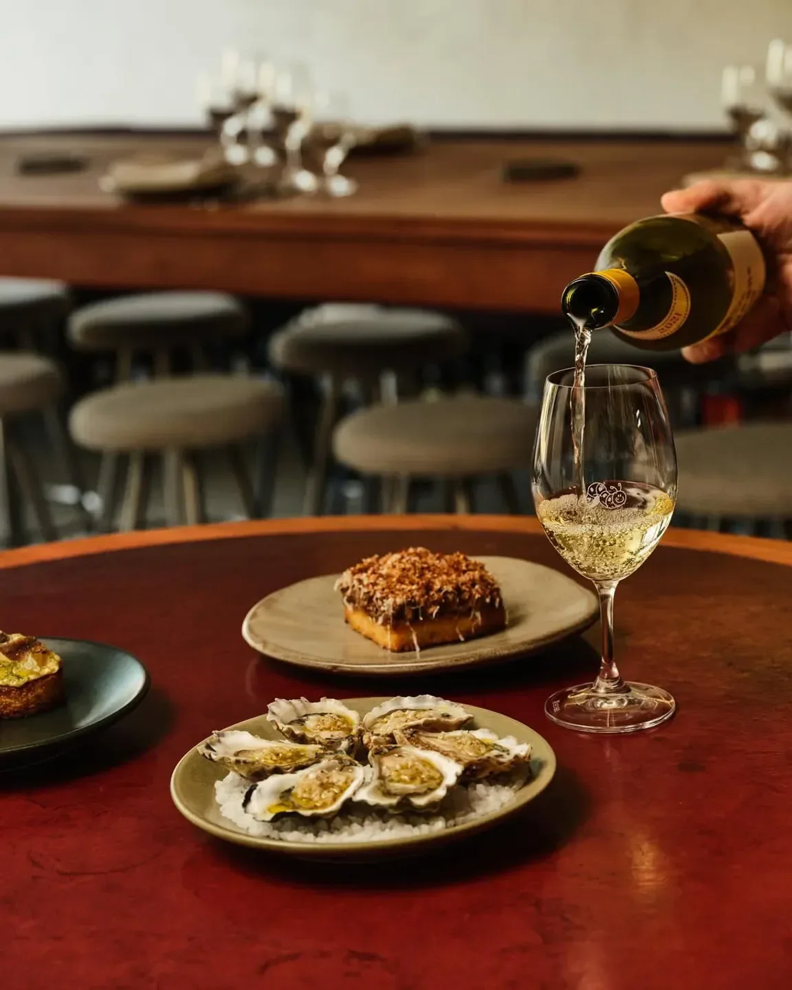 Wine being poured at Clover restaurant in Melbourne, alongside fresh oysters and dessert.