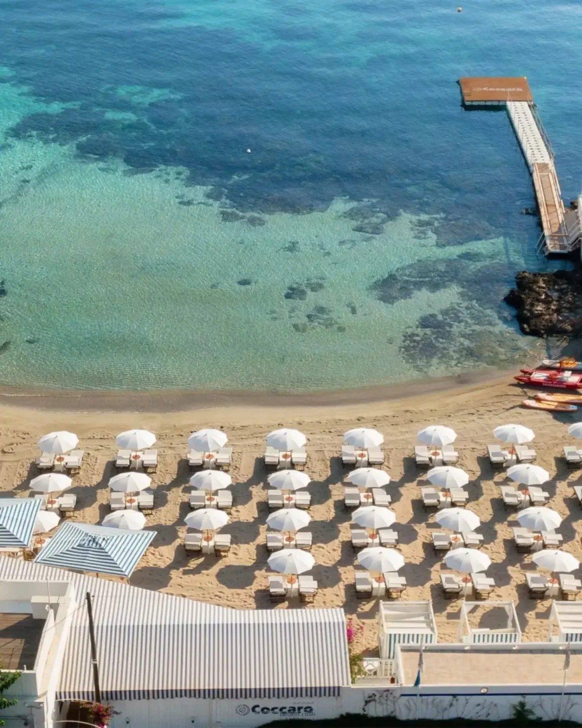 Coccaro Beach Club in Puglia offers pristine beach with rows of sun loungers and umbrellas overlooking clear blue water.