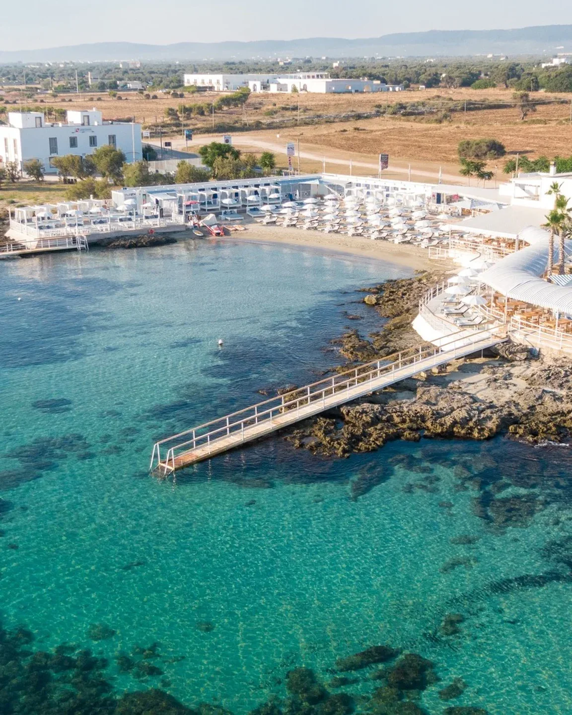 Coccaro Beach Club in Puglia features a stunning white resort with sun loungers and clear turquoise waters.