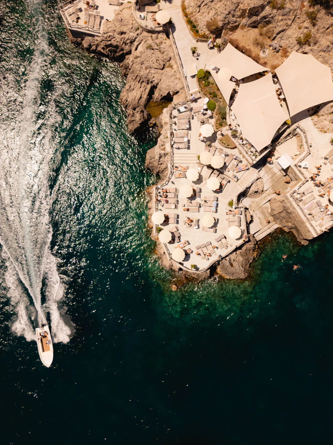 Aerial view of Conca del Sogno beach club on Amalfi Coast with sunbathers and a boat in the clear blue water