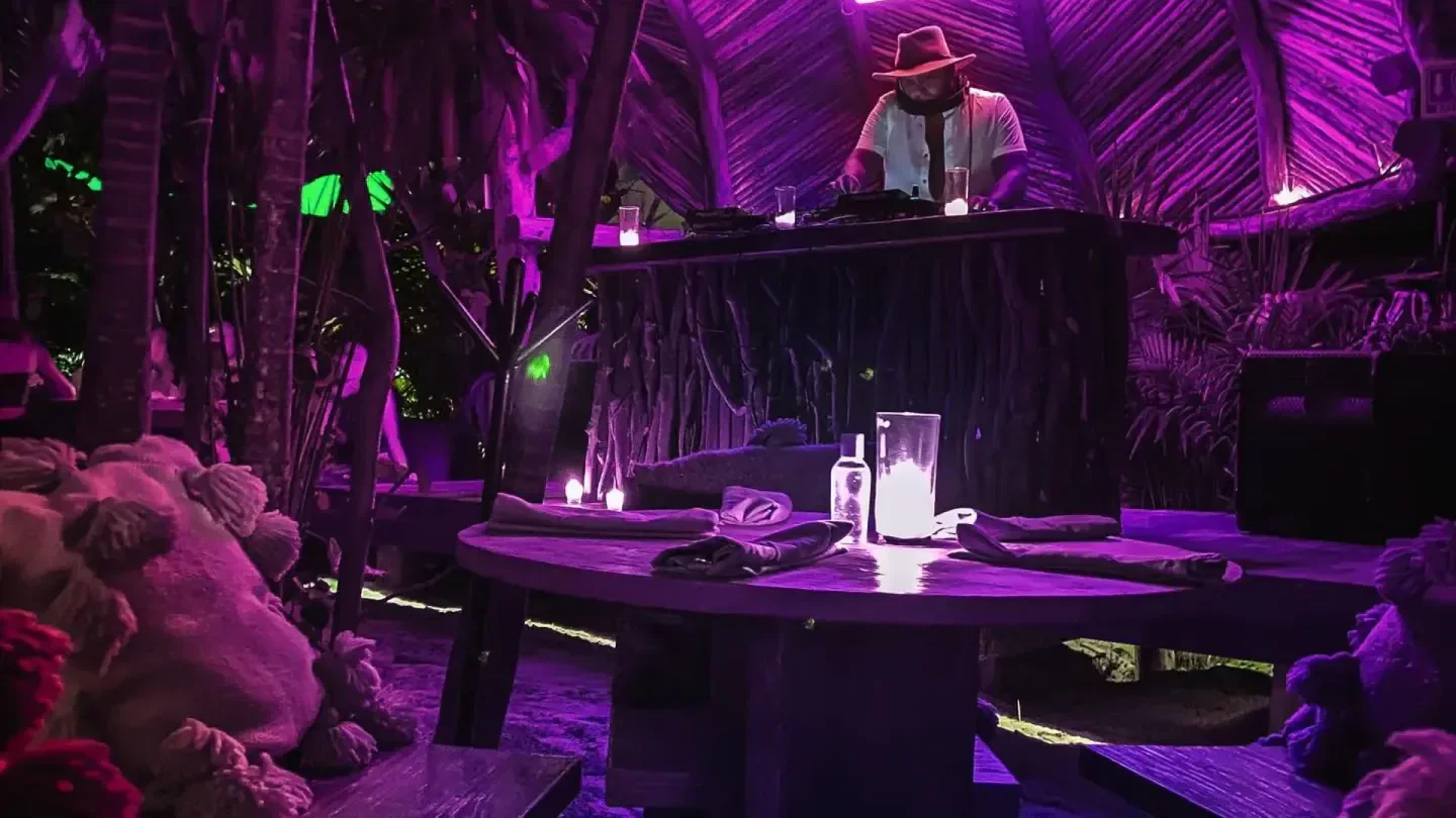 DJ playing at Confessions nightclub in Tulum, surrounded by lush, purple-lit tropical decor