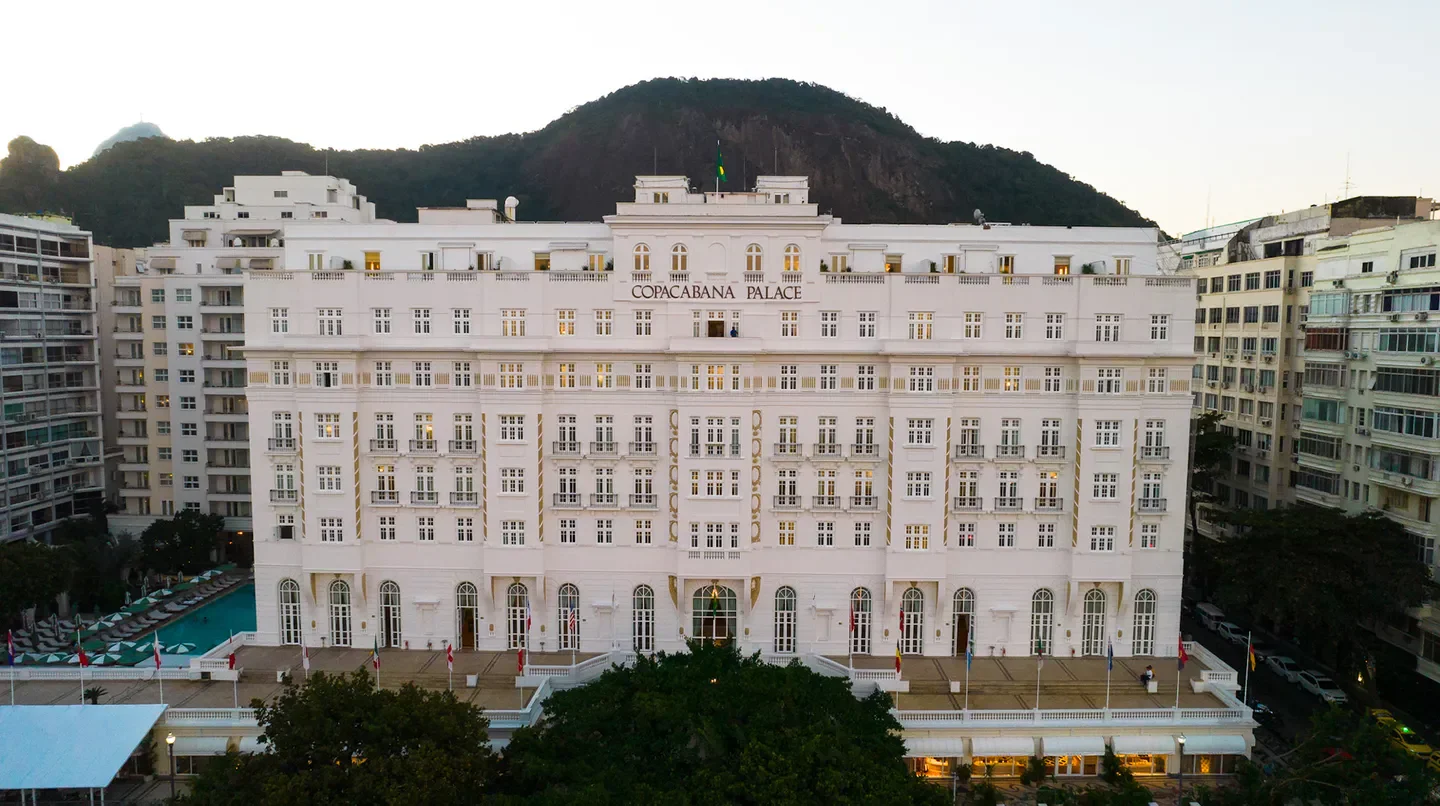 Exterior view of Copacabana Palace, A Belmond Hotel, Rio de Janeiro, with mountain backdrop.