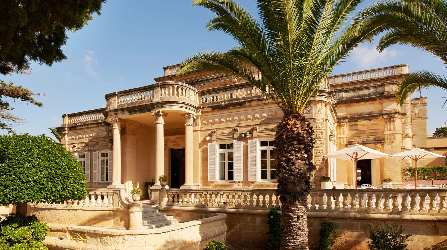 Exterior of Corinthia Palace Malta hotel in Malta, showcasing a classic facade and palm trees.