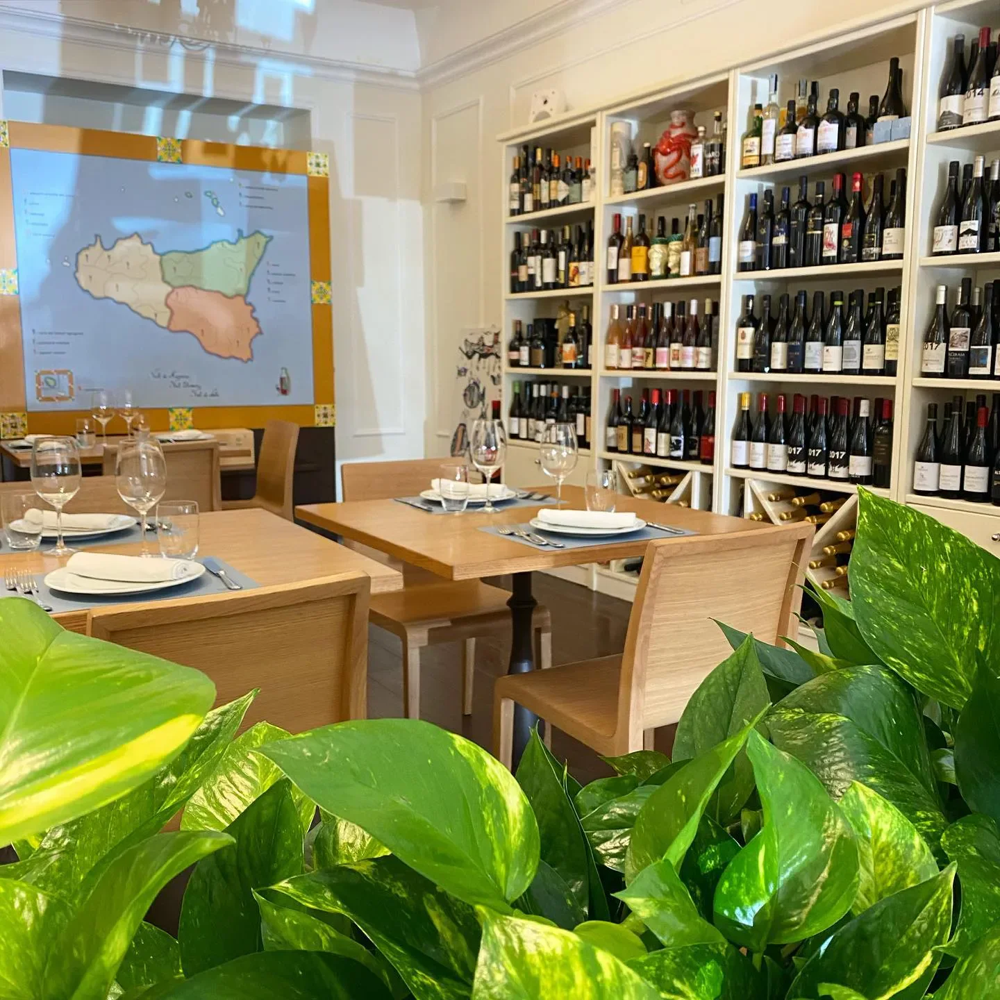 Interior of Corona Trattoria in Sicily, with tables set and shelves of wine.