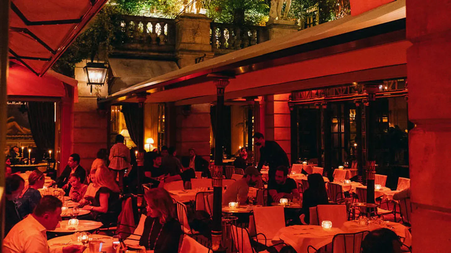 Costes Paris restaurant interior, featuring a red-lit dining area with guests at tables.