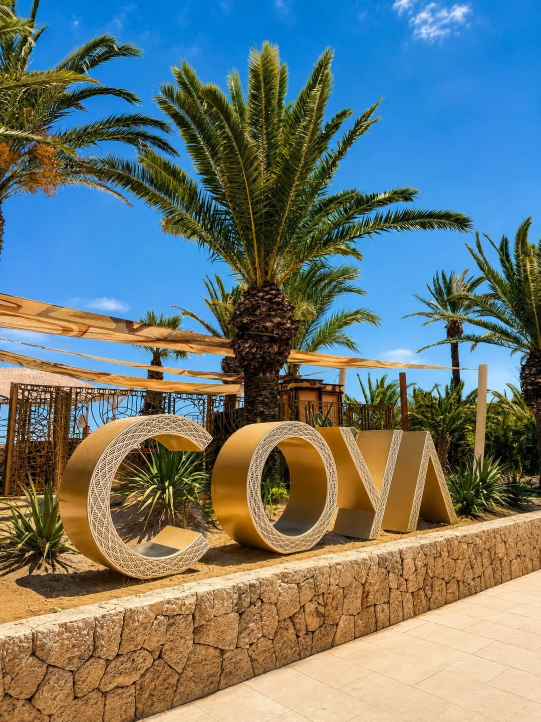 COYA Beach entrance with large gold letters and palm trees under a blue sky.