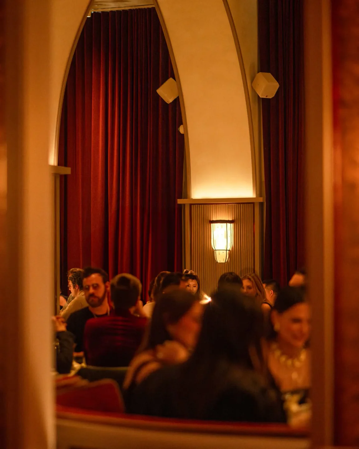 Dimly lit dining room at Crane Club, with guests seated under red velvet curtains and ornate lighting.