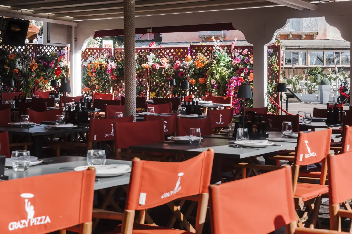 Bright and vibrant outdoor seating area at Crazy Pizza Porto Cervo with red chairs and floral decorations