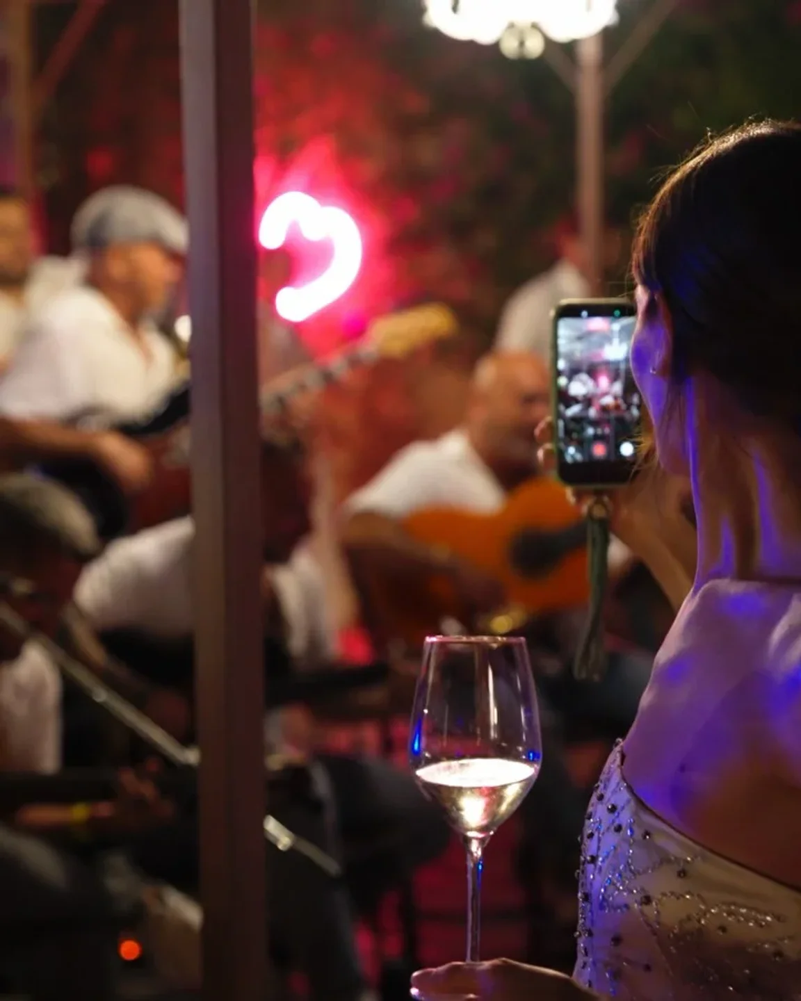 Woman films live band performance with wine glass at CUE restaurant in Porto Cervo.
