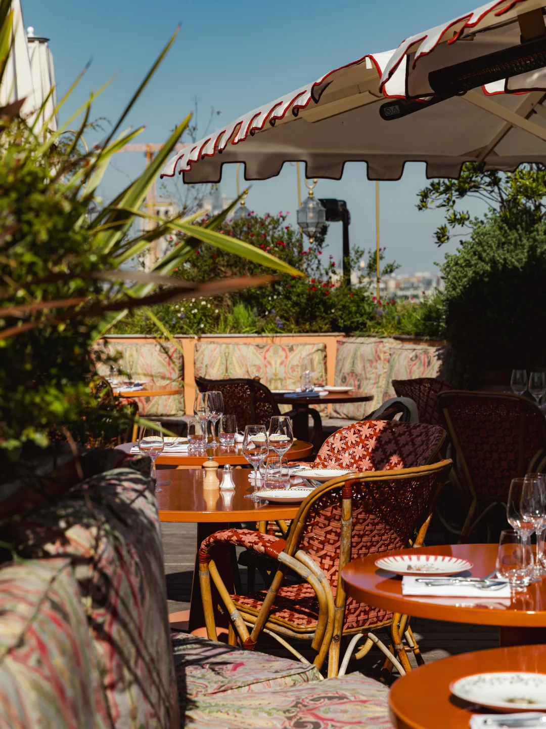 Dar Mima Paris rooftop terrace with tables set for dining amidst lush greenery and cityscape views.